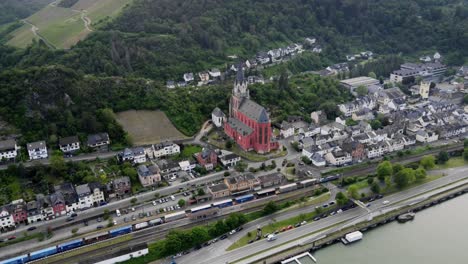 freight train transporting cargo through oberwesel town past red church of our lady along river rhine