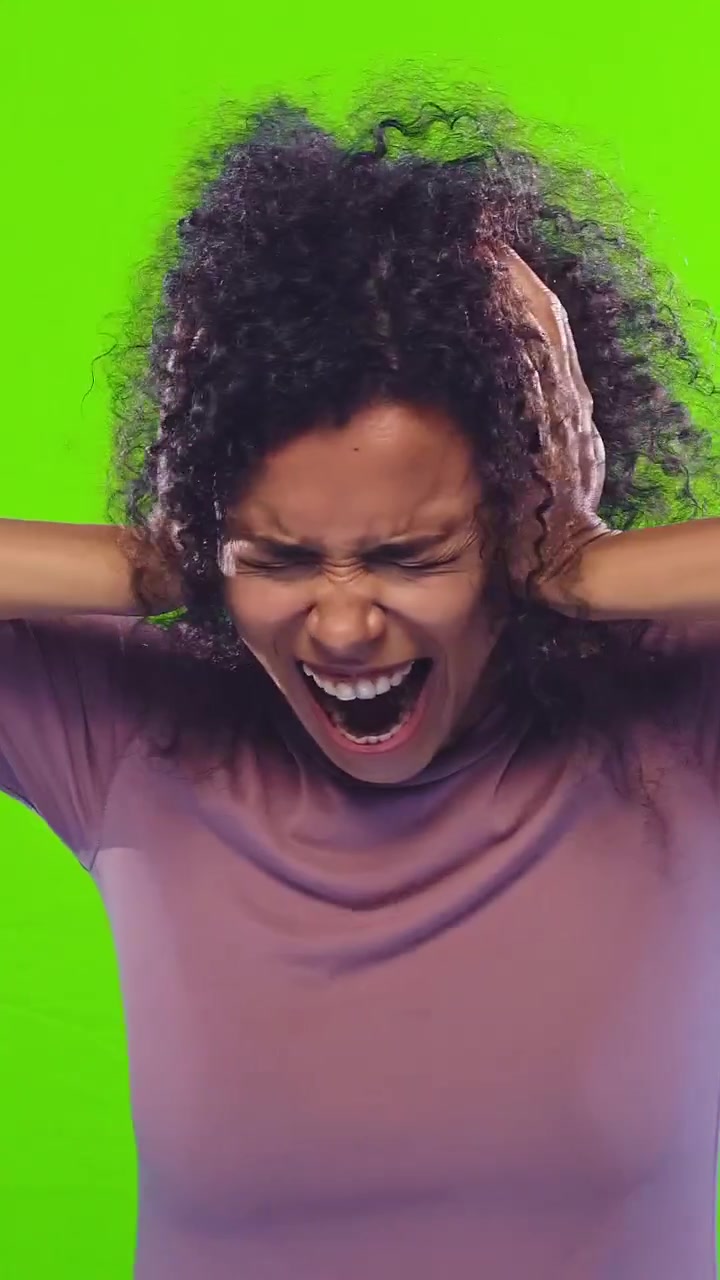Young woman covering ears and screaming in frustration against green background