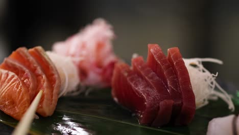 detailed view of salmon and tuna sashimi artfully arranged on a green leaf with garnish.