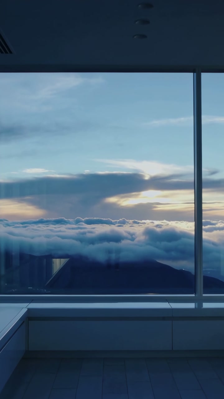 Vertical video: Large window view showing low clouds shifting over peak during sunrise in high room
