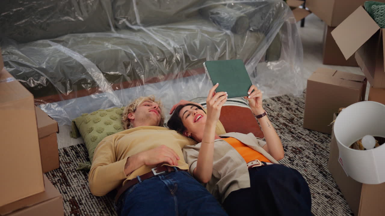 Happy Young Couple Relaxing on Floor with Tablet Amidst Moving Boxes