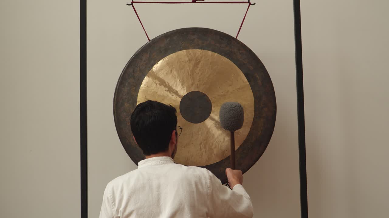 Male musician playing Gong with his back turned to camera