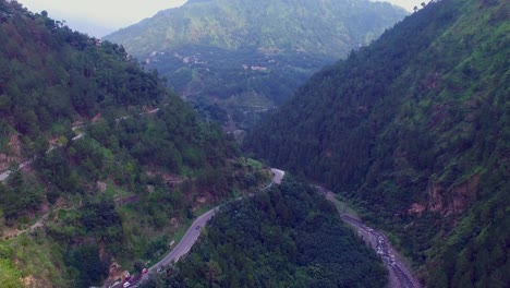 Vuelo-Aéreo-Sobre-Montañas-Frescas,-Ríos-Y-Praderas,-Conducción-De-Automóviles-A-Lo-Largo-De-La-Carretera-Rodeada-De-Bosques,-Un-Poste-De-Alta-Transmisión-Eléctrica-Que-Se-Muestra-En-Los-árboles-Para-Distribuir-Casas-En-Las-Montañas