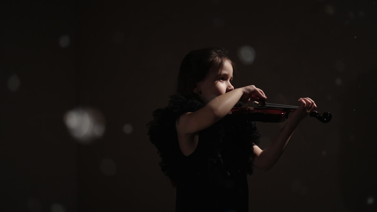Giovane ragazza che suona il violino in uno studio buio