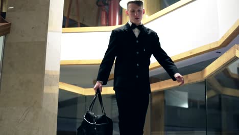 Young-businessman-in-a-suit-with-a-bowtie-is-going-down-the-stairs-holding-big-black-leather-bag.-Slow-Motion