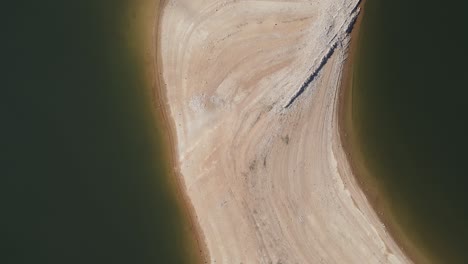 a top-down aerial view showcasing a curved sandy shoreline meeting dark, calm water