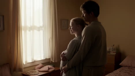 intimate moment of an expecting couple embracing by a window