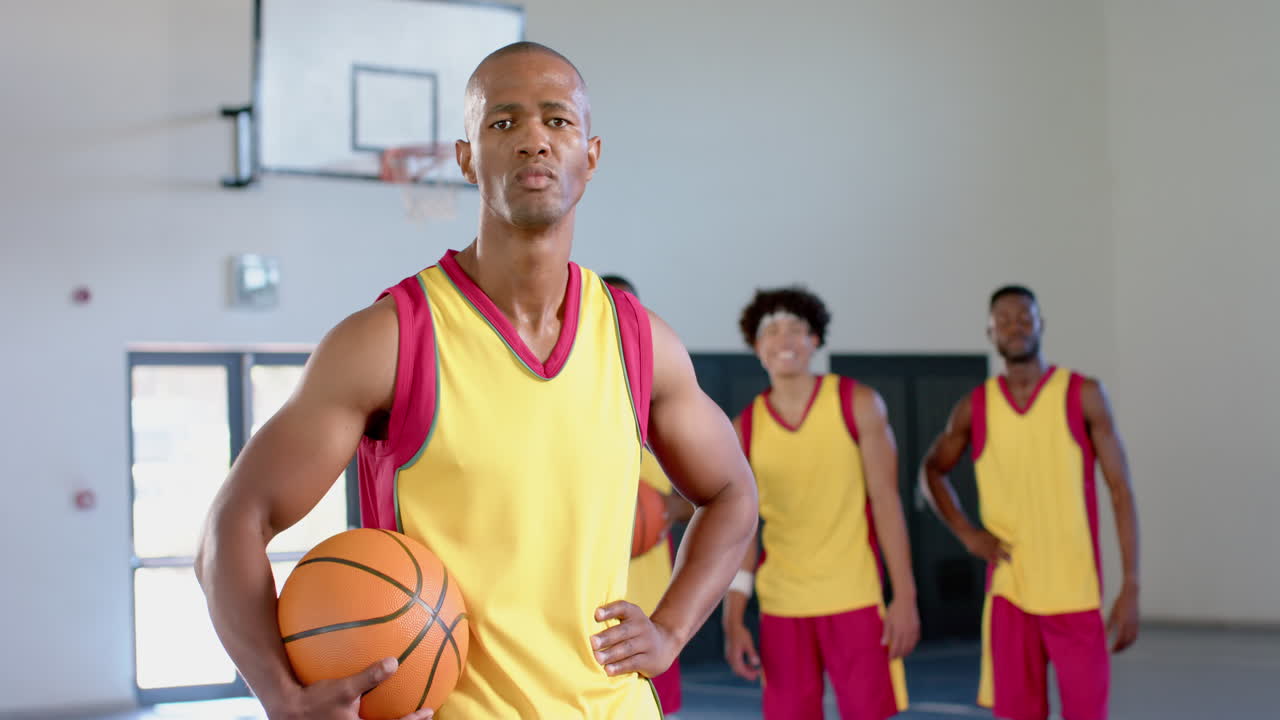 Hombre afroamericano sostiene un balón de baloncesto en un gimnasio.