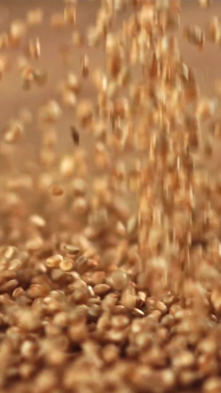 Primo piano al rallentatore di chicchi di quinoa che cadono su una superficie in legno