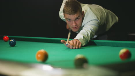 close-up of focused player in white shirt leaning over green pool table, striking white billiard ball with cue stick. intense gaze and precise aim capture skill, concentration in competitive billiards