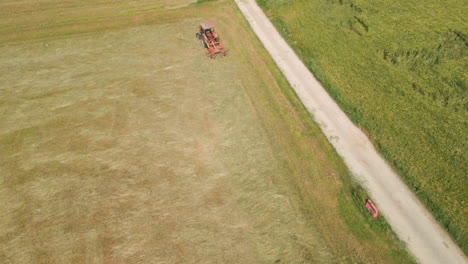 top view of a working tractor with spinning mechanical rake on freshly cut hay fields at summer in northern italy
