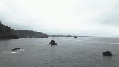 Hovering-above-the-rugged,-rocky-Oregon-coast,-USA,-an-aerial-view-reveals-its-captivating-natural-allure,-where-the-land-converges-with-the-sea