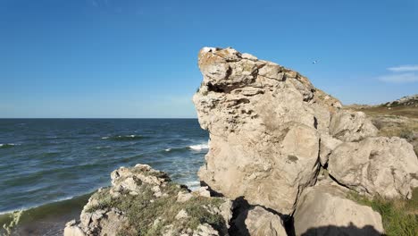 A-striking-rock-formation-juts-out-from-the-shoreline,-contrasting-against-the-blue-waters-of-the-Sea-of-Azov-under-a-clear-sky-in-Crimea