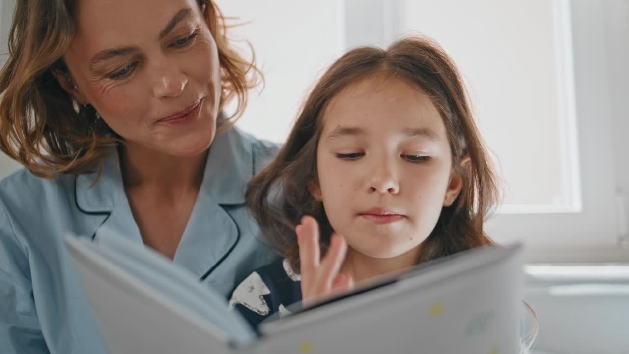 Woman parent daughter reading book sitting bed closeup. Mother daughter morning