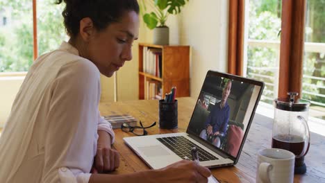 Mujer-Afroamericana-Tomando-Notas-Mientras-Realiza-Una-Videollamada-En-Una-Computadora-Portátil-En-Casa