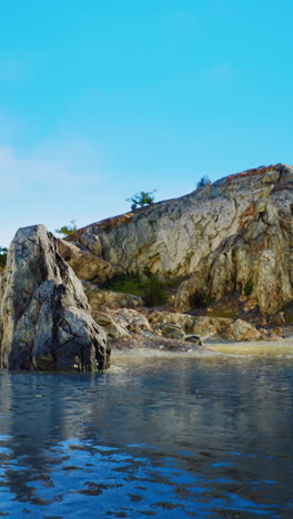 a lone rock stands in a small body of water with a mountain behind it.