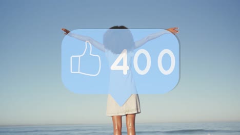 Animation-of-speech-bubble-with-thumbs-up-icon-and-numbers-over-woman-with-arms-stretched-on-beach