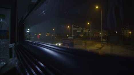 looking out the window of a train, it's night, the many lights brighten the darkness up, coloring the scenery