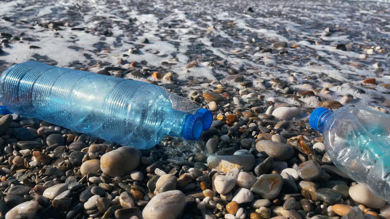 primer plano de botellas de plástico en las olas, rodeadas de espuma y rocas