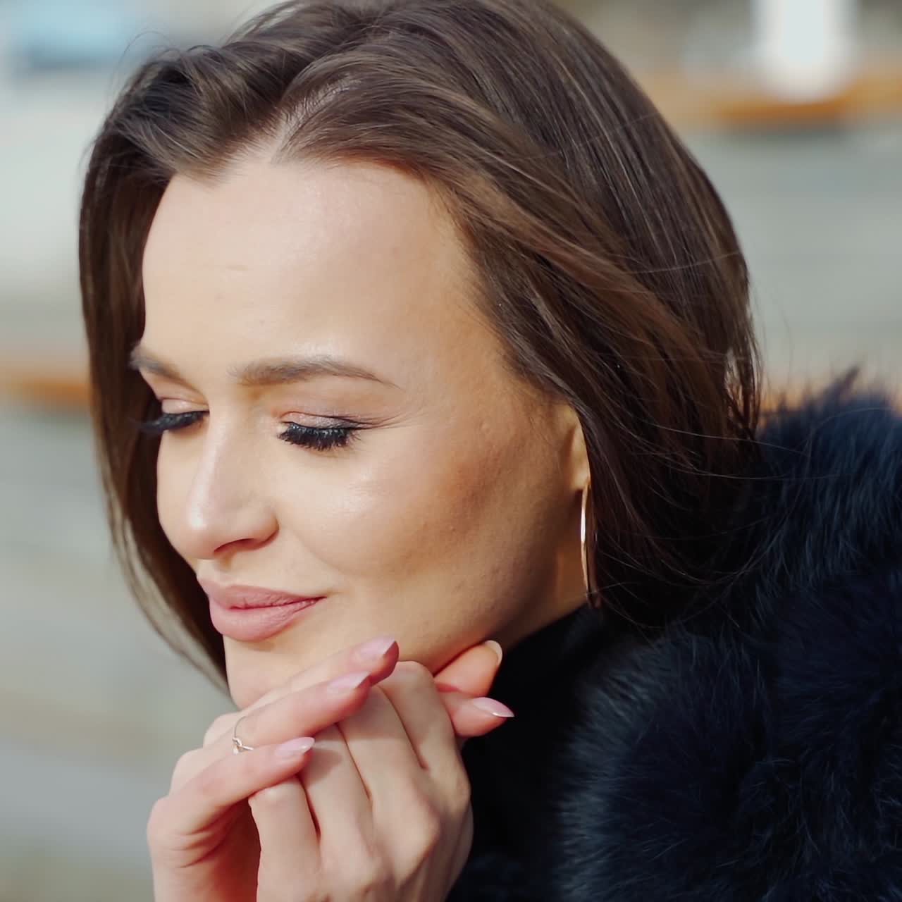 Portrait of attractive smiling brunette. Pretty face of a young woman in fur coat sitting outdoors and looking on camera. Close-up.