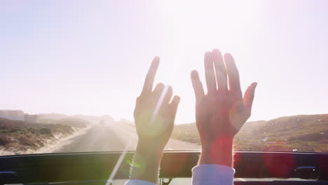 Young-couple-driving-reaching-hands-out-through-car-sunroof