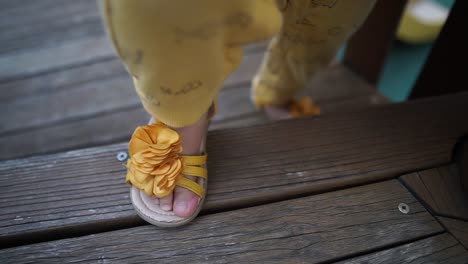 legs and tiny feet of a baby girl wearing yellow sandals climb on wooden steps at playground. - close up
