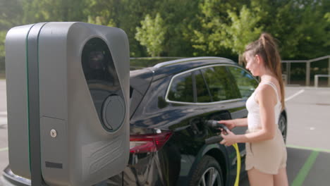 chica conectando un coche eléctrico y una estación de carga con un cargador de cable
