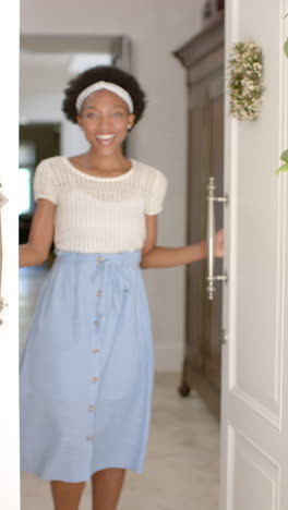 vertical video of portrait of happy african american woman opening door, in slow motion