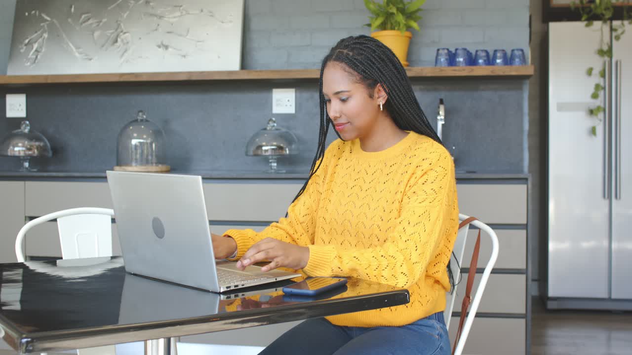 Woman placing hands on laptop, typing, glancing at smartphone and notebook for kitchen work