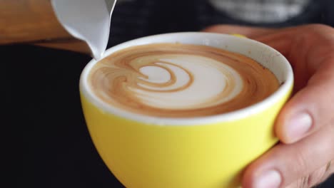 un habilidoso barista sirviendo un latte art con diseño de rosetta en una taza de café amarilla | cafetería gourmet | filmado en hd a 24 fps cinemáticos