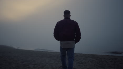 young man walking on sandy beach in morning fog. lonely guy looking sea horizon