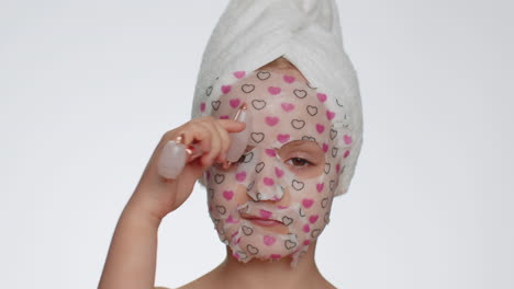 Beautiful-young-smiling-child-girl-applying-cosmetic-moisturizing-face-mask,-use-massage-roller