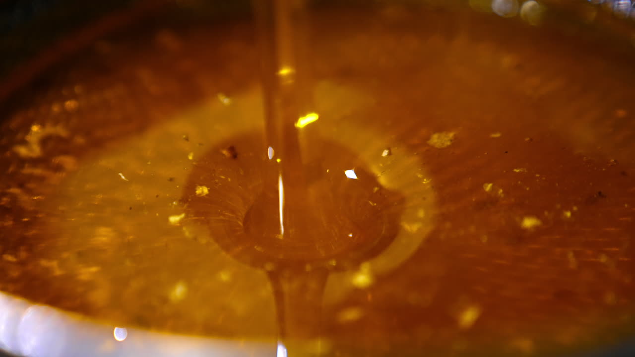 Amber honey flowing into the dish. Beautiful fresh organic product being poured onto the metal sieve for cleansing.