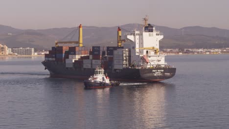 loaded container ship pulled by tug into algeciras port