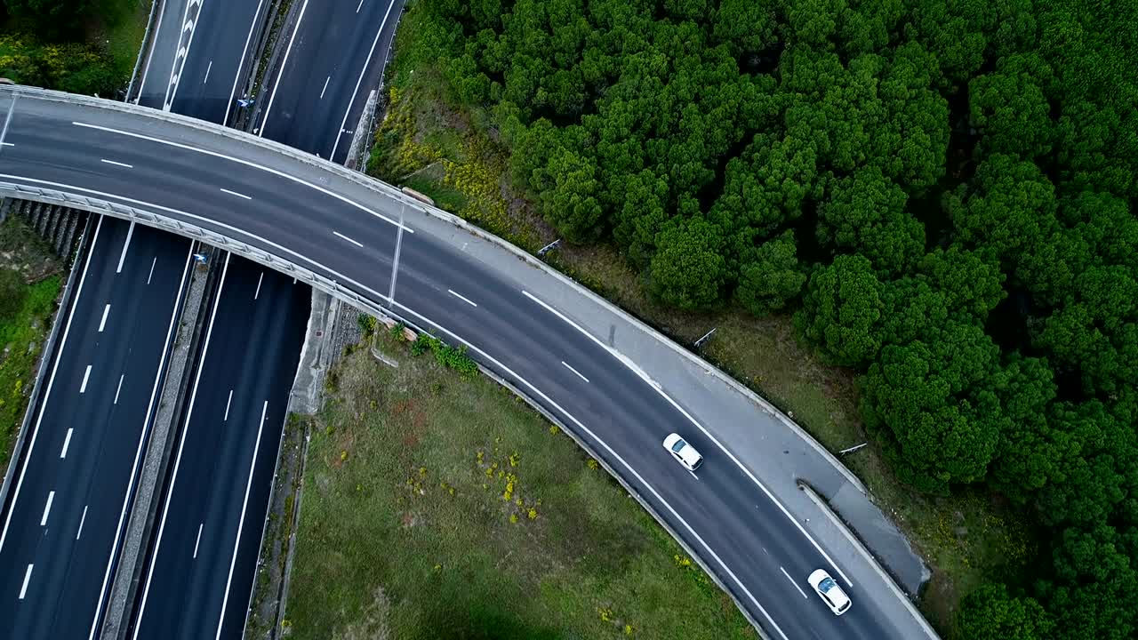 Aerial view over road bridge on highway interchange in France. Only homes and grass fields around roads. Cars and trucks driving on the roads.