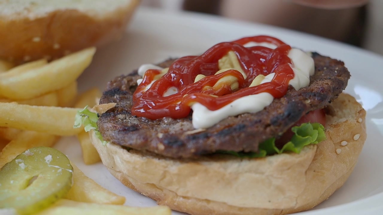 Ketchup che viene spremuto su un hamburger di manzo alla griglia