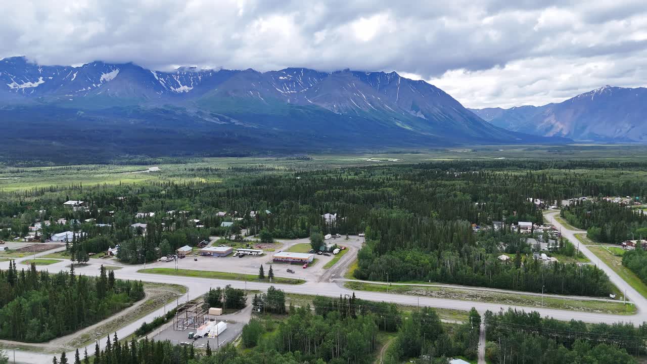 Serene aerial drone footage captures remote Alaskan town nestled against majestic snow-capped mountains and vast evergreen forests