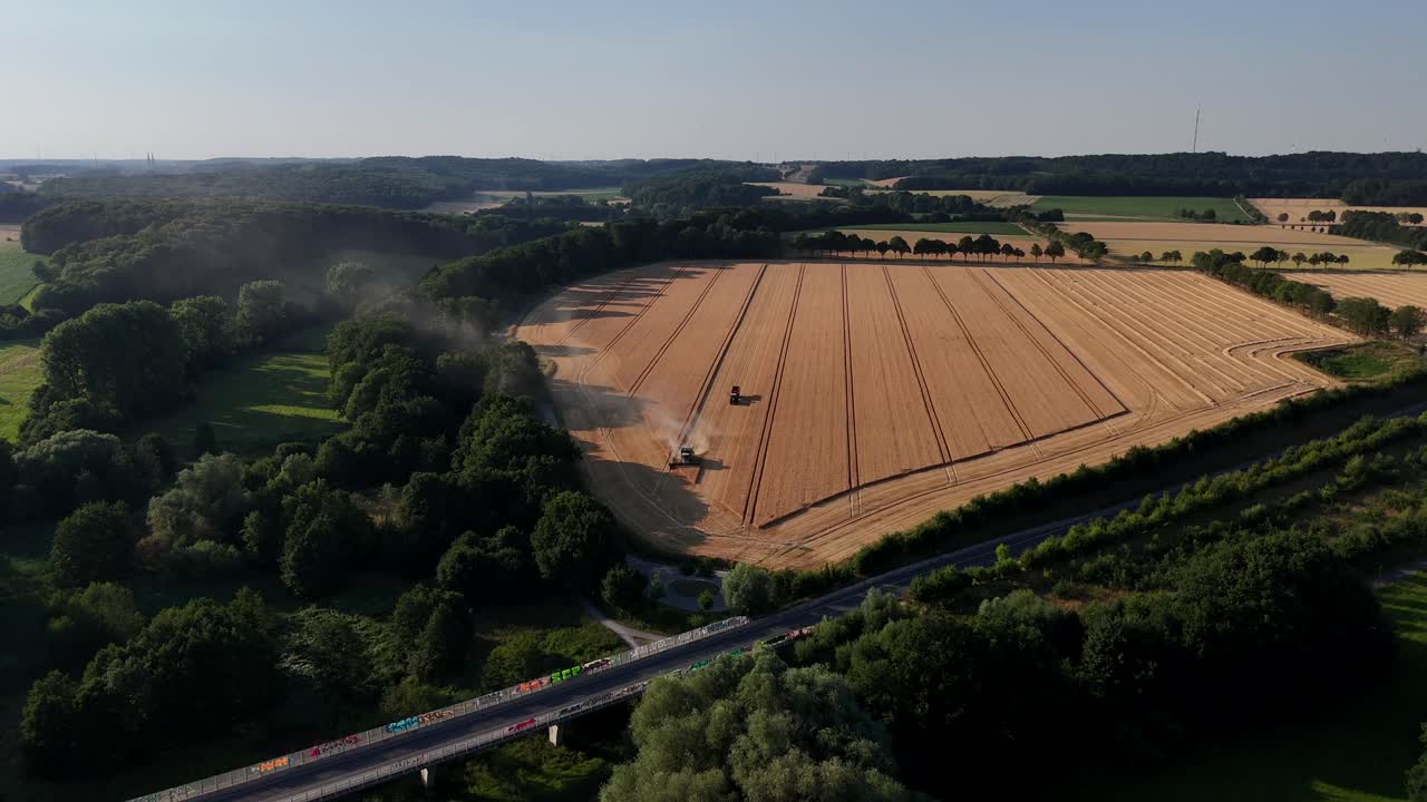 Luftfoto af amerikansk landbrugsland om sommeren med gyldne hvedemarker, mejetærskere i arbejde, skovkanter og motorvej i forgrunden. Klassisk landskab med aktivt landbrug og vide horisonter, USA