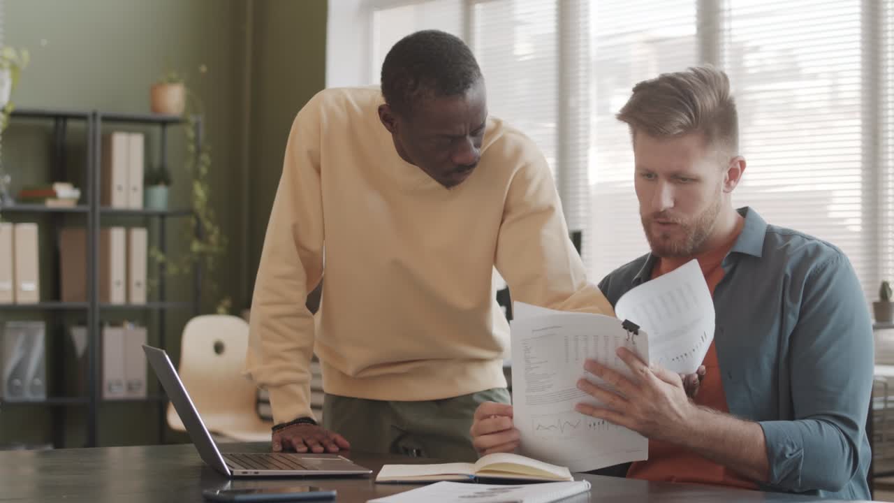 Two Diverse Colleagues Analyzing Financial Documents in Office
