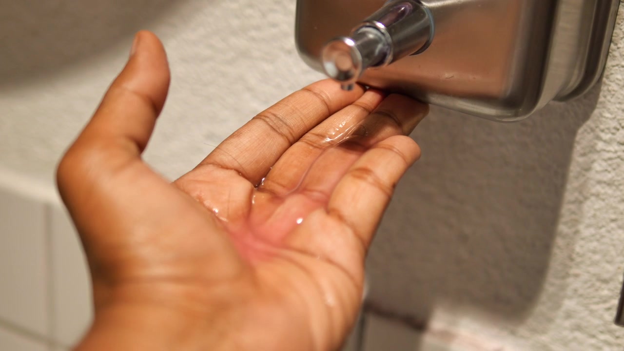Persona che eroga sapone liquido da un dispenser a muro
