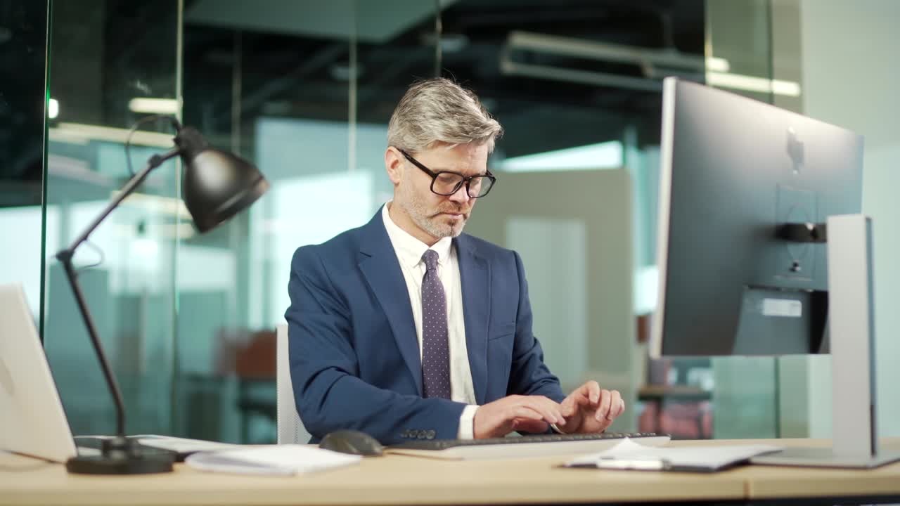 Portrait thoughtful male businessman working on pc computer at a modern office desk. Confident Focused pensive business man employee in suit indoor