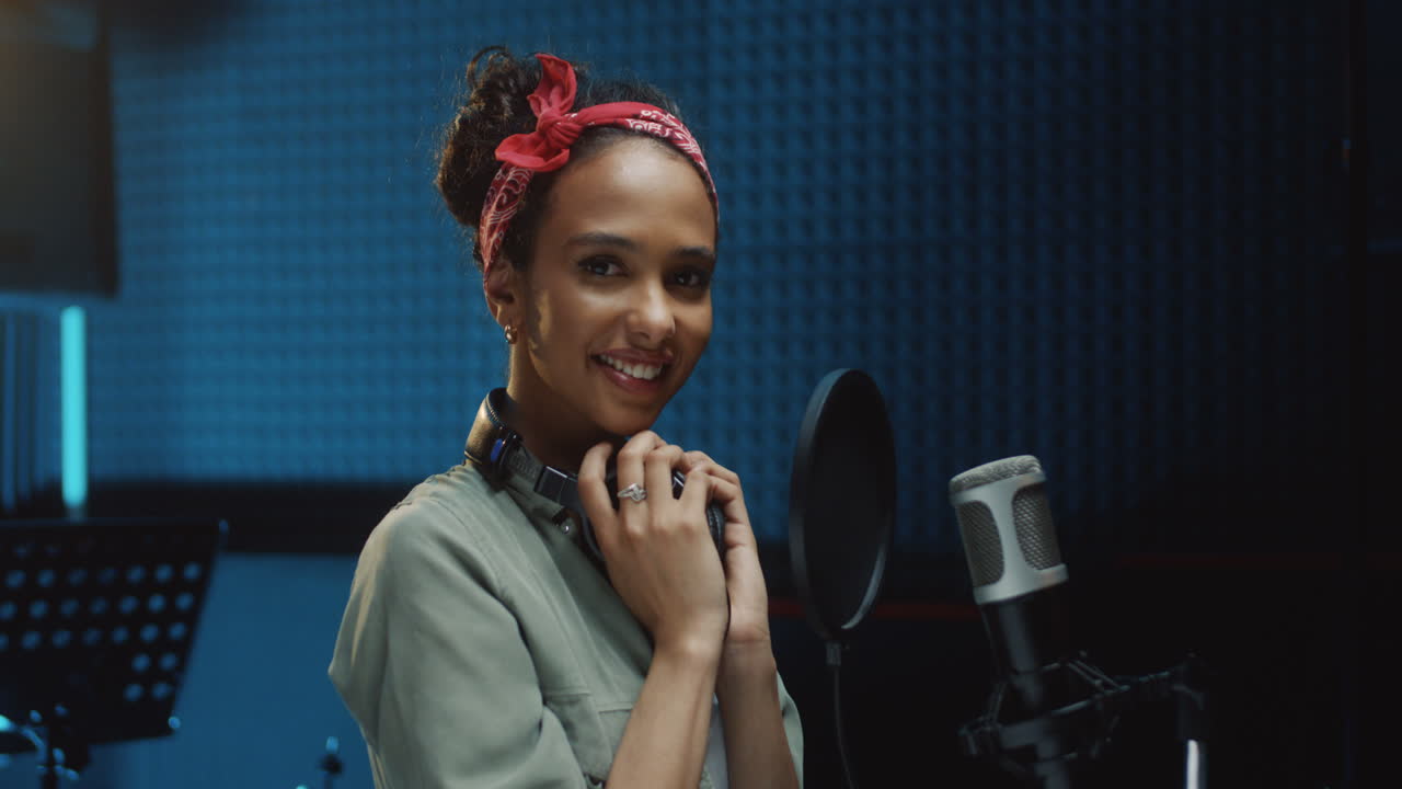joven y hermosa cantante alegre quitándose los auriculares y sonriendo a la cámara después de grabar una canción en el estudio de sonido