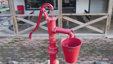 una vieja bomba de agua roja con un balde colgando de ella