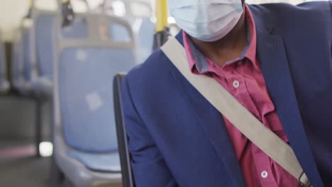 hombre afroamericano con máscara facial usando un teléfono inteligente con pasaporte covid en el autobús