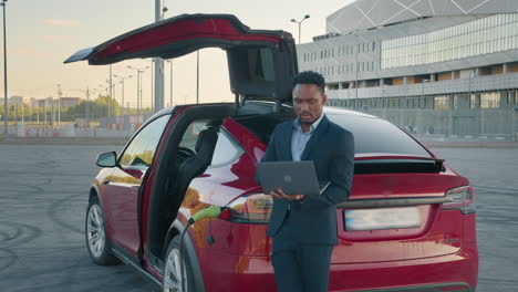 hombre de negocios usando una computadora portátil cerca de un coche eléctrico