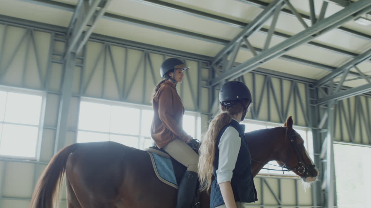 Two people, one riding a horse and another leading, in an indoor equestrian arena