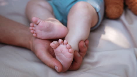 dad's hand holding tenderly a tiny baby foot. infant tossing his feet as father touches them. close up.