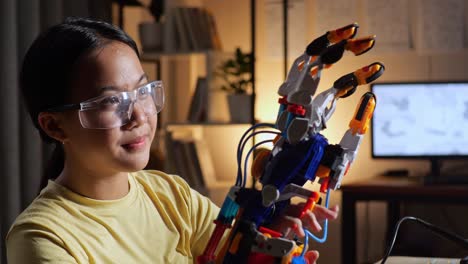 close up of satisfied teen asian girl looking and checking a cyborg hand while working on a laptop at home