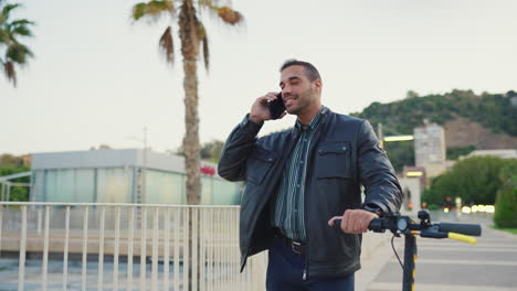 Young-man-with-scooter-calling-on-smartphone-outdoors.