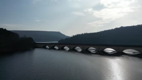 aerial drone flight over ladybower reservoir slowly flying under the bridge to reveal the woodlands